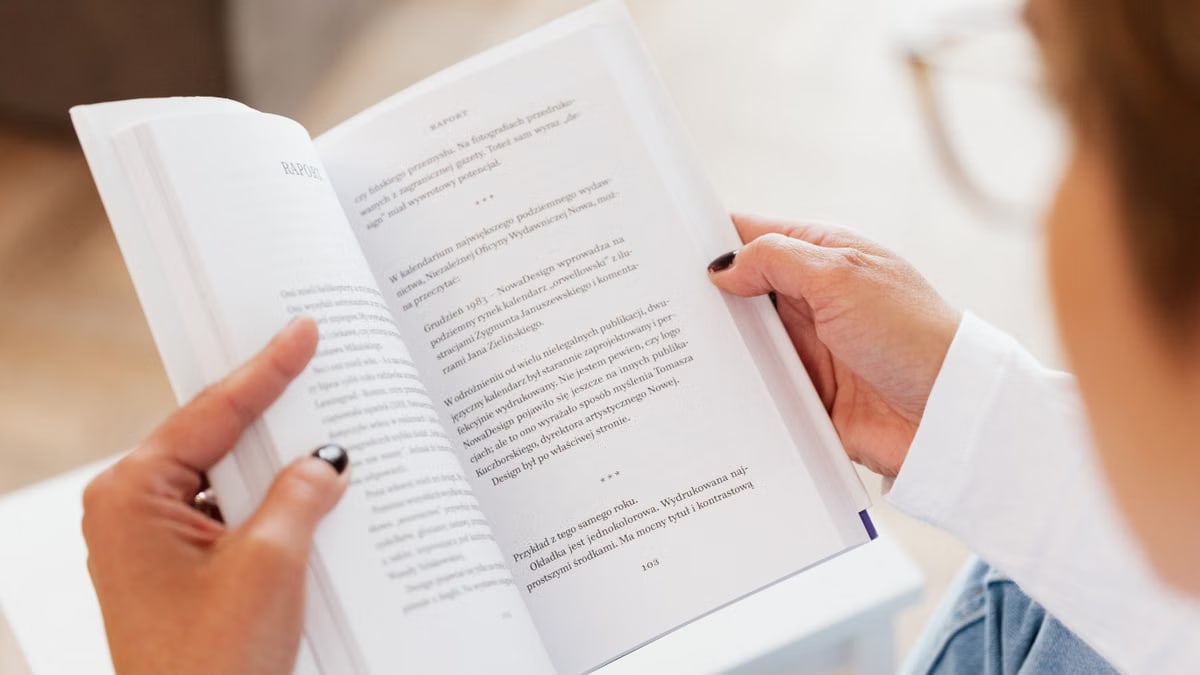 From above anonymous female in white shirt and jeans reading book while sitting at small white tea table